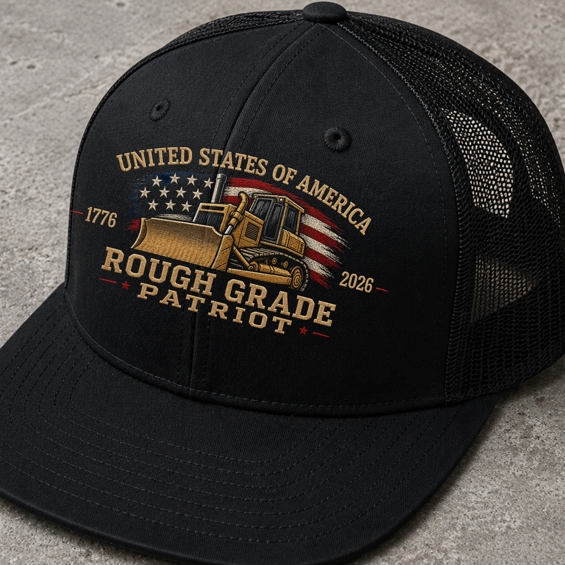 Black trucker hat with 'Rough Grade Patriot' design on a gray surface